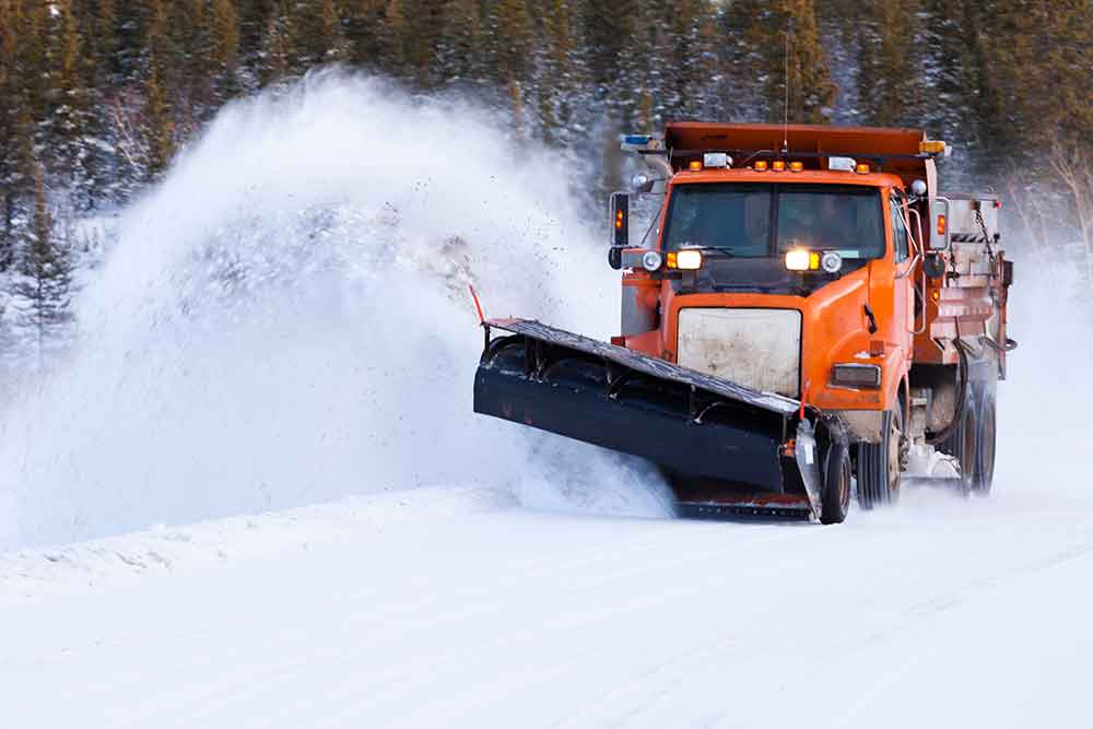 Orange snow-removal truck blowing snow off a road after a winter storm