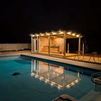 Wooden poolside cabana with LED lighting glowing over a swimming pool at night