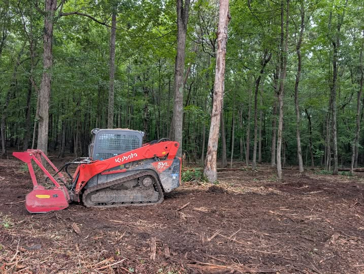 Kubota track loader with forestry mulcher head clearing underbrush in a wooded lot
