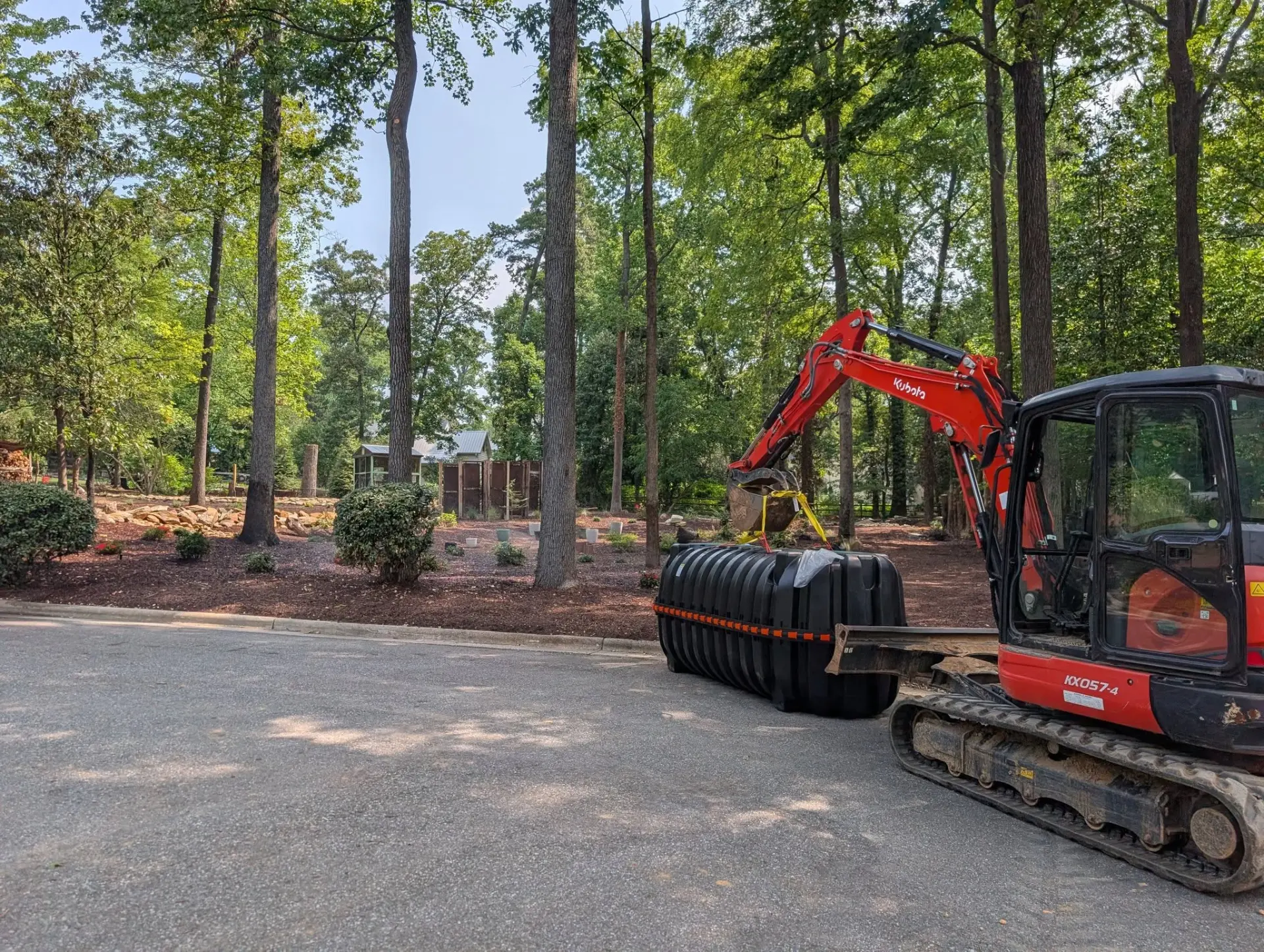 Kubota mini excavator setting a septic tank in a landscaped yard