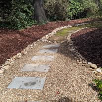 Stepping stone walkway with gravel and river rock borders through mulched beds