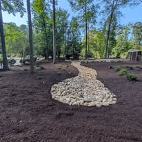 River rock dry creek bed drainage swale winding through fresh mulch beds